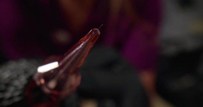 Slow motion close up of tattoo machine needle puncturing skin in tattoo studio with artist in background.