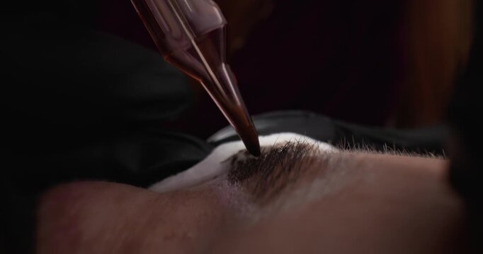 Permanent makeup microblading tool applying pigment to eyebrow on client in beauty studio.