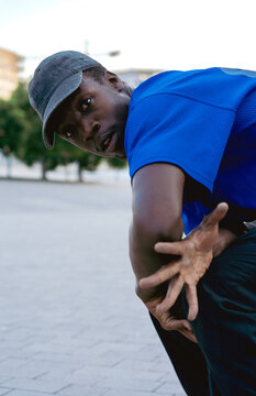 Young Black dancer performing a street dance move, bending down and looking intently at the camera outdoors