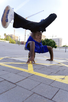 Male breakdancer balancing on his head and hands, practicing street dance acrobatics in a city square