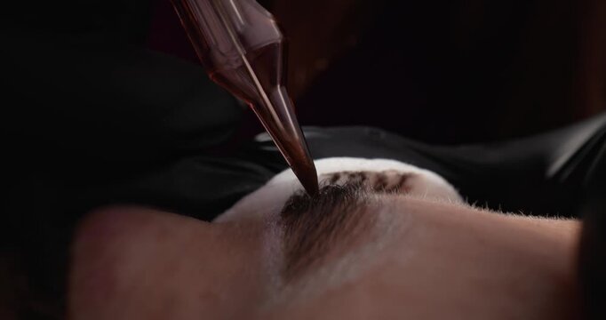 Macro shot of technician applying permanent makeup eyebrow pigment to client in beauty studio.