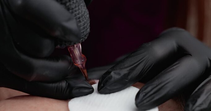 Slow motion tattoo artist applying ink to client's skin in tattoo studio closeup tracking shot.