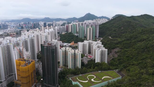 Aerial view of high-rise residential buildings and green rooftop with wavy patterns next to mountain in Hong Kong.