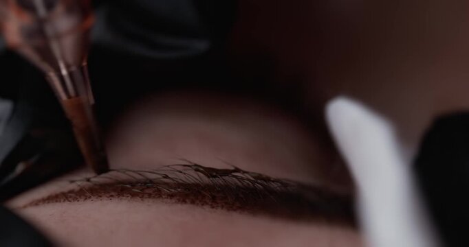 Closeup of client eyebrow micropigmentation being applied by technician in beauty clinic on brow area. Macro permanent makeup process.