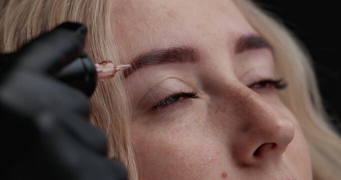 Closeup slow motion of microblading eyebrow tattooing on female client face in beauty studio handheld tracking movement.