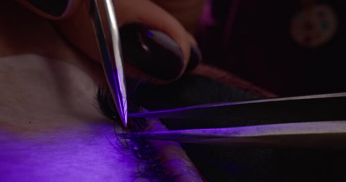 Probe macro eyelash extension application on client's closed eye in salon treatment bed.