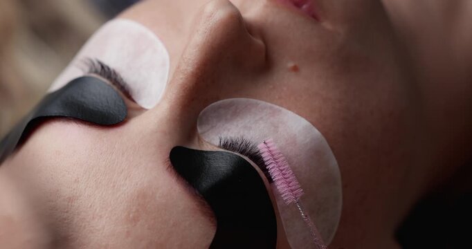 Slow motion close up of eyelash brushing and application during eyelash extension treatment in beauty studio.