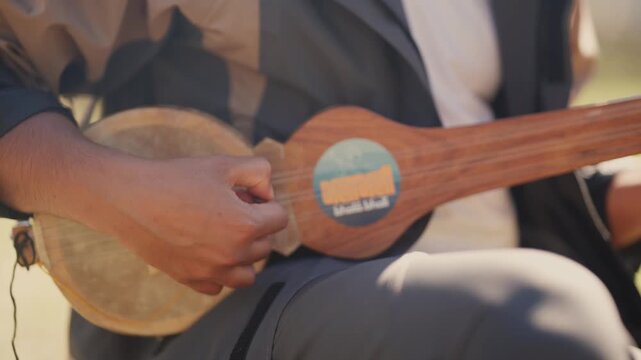 Close-up side angle of a Himalayan musician strumming a handmade wooden lute with visible string detail and warm afternoon light