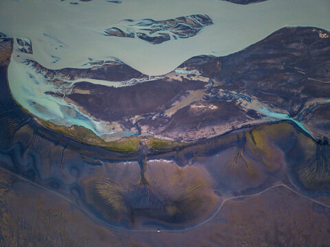 Aerial view of a glacial river delta with intricate sediment patterns and braided channels flowing through the volcanic landscape of Iceland.