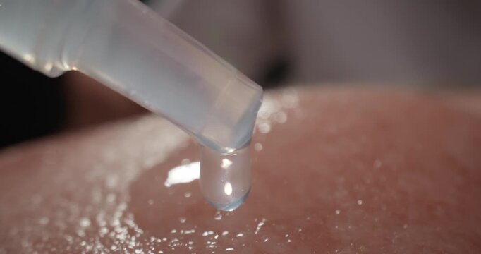 Slow motion dropper releasing serum onto facial cheek skin close up studio setting, macro.