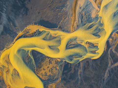 Aerial view of a braided river with golden sediment flowing through a dark volcanic landscape in Iceland.
