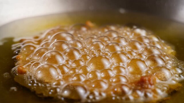 Slow motion close up zoom of breaded cutlet frying and bubbling in hot oil in pan on stovetop in kitchen