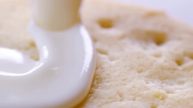 Slow motion close up macro of white cream pouring and spreading over crunchy round biscuit on kitchen countertop surface