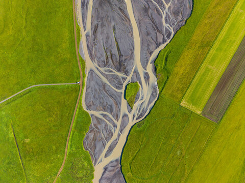 Aerial view of a braided river with dark sediment and winding water channels flowing through vibrant green fields in Iceland.