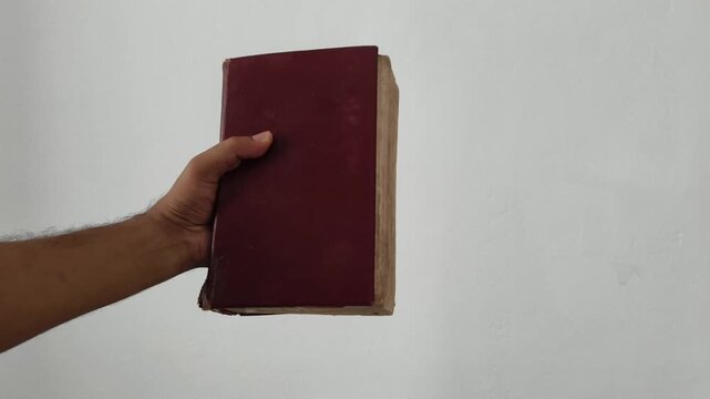 Closeup of person hand holding closed ancient, antique, old, or vintage shabby holy bible book with leather cover isolated on white background with copy space. Historical knowledge exploration concept