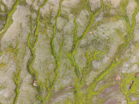 Aerial view of vibrant green mossy patterns and intricate river channels winding through the volcanic landscape of Iceland.