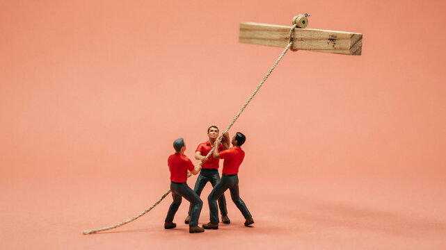 Tiny construction workers pulling a rope together to lift a heavy wooden beam against a warm colored background with construction, miniature