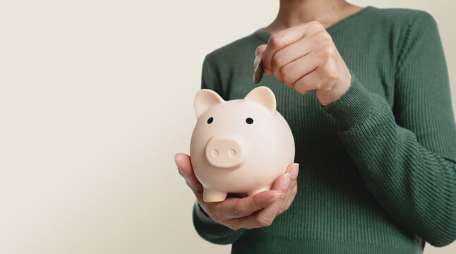 Female hands putting a coin into a piggy bank. Symbolizing saving money, budgeting, personal finance, financial planning and future financial security.