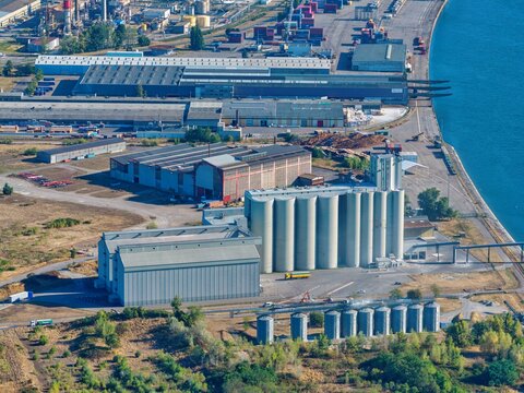 Aerial view of the industrial site with large grain silos, warehouses, and storage facilities located along the waterfront in Hombourg, Grand Est, France.