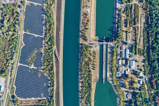 Aerial view of a large solar farm situated next to a canal and a lock system in Hombourg, Grand Est, France.