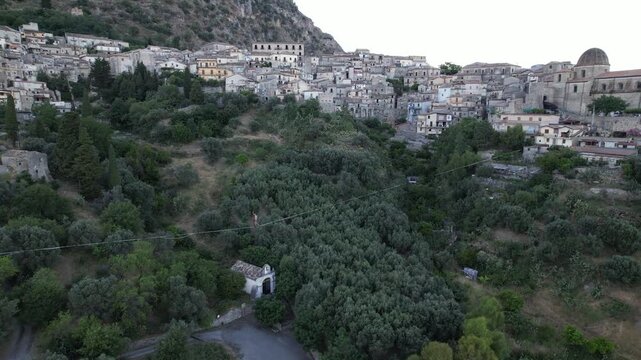 An aerial view of a tightrope walker walking above a deep valley. The tightrope walker carefully balances on the rope above a lush green canyon and olive trees. Italy. Stilo, August 15, 2026.