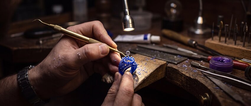 A close up view of the artisan hands sculpting a detailed blue wax ring, highlighting the intricate craftsmanship involved in jewelry making