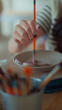 Female potter painting handmade ceramic bowl with brush in pottery studio, close up of artisan craftsmanship and creative process