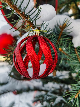 A red ornament hangs from a natural Christmas tree surrounded by snow. The tree features various decorations celebrating New Year and Christmas