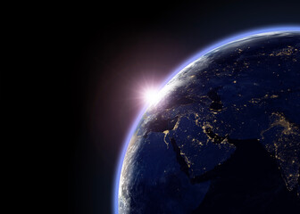 Earth and sunlight viewed from outer space, showing the planet’s illuminated horizon and city lights across the night side. © Chandet