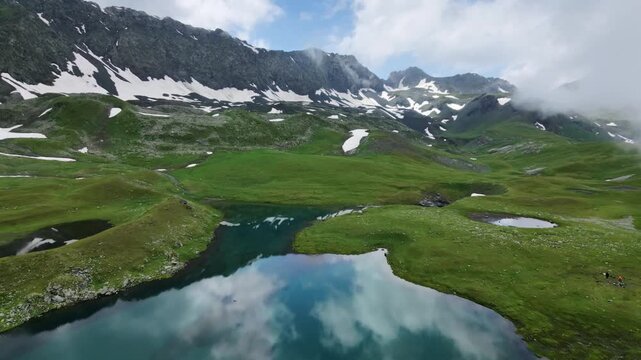 Aerial view of a wild camping site with tents by a turquoise mountain lake under a cloudy sky