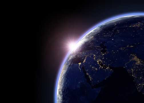 Earth and sunlight viewed from outer space, showing the planet&rsquo;s illuminated horizon and city lights across the night side.