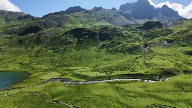 Scenic aerial view of a mountain valley with a winding stream flowing into a lake near a remote campsite