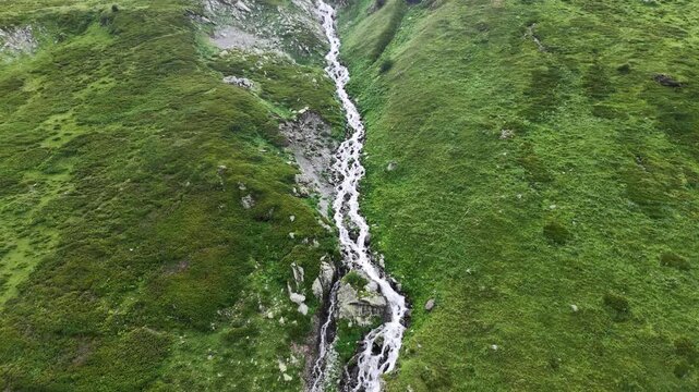 Aerial view of a fast flowing mountain stream and small waterfalls cascading down a lush green slope.