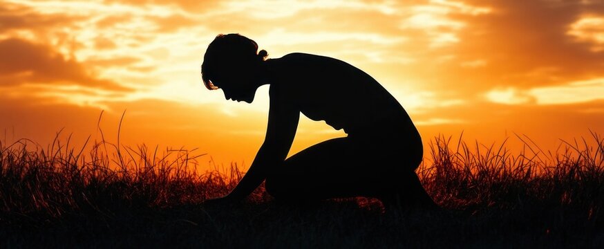 silhouette of a person kneeling in tall grass at sunset with warm orange sky, contemplative and peaceful mood