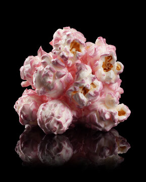 Pink glazed popcorn kernel cluster isolated on black backdrop, concept of sweet snack creativity and playful food art