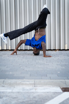 Energetic Black man breakdancing headstand on urban street pavement, demonstrating power and agility
