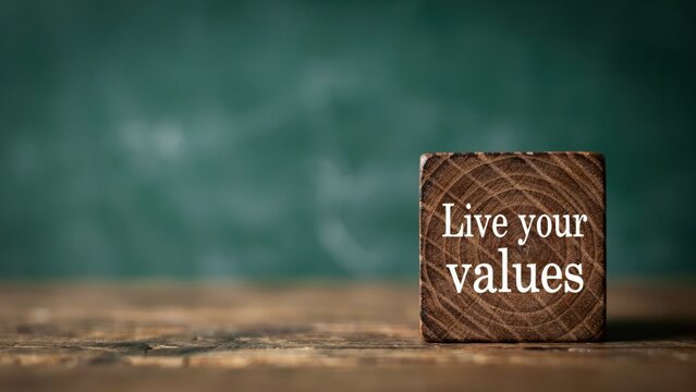 Wooden block with "Live your values" text on a rustic table with a blurry green background