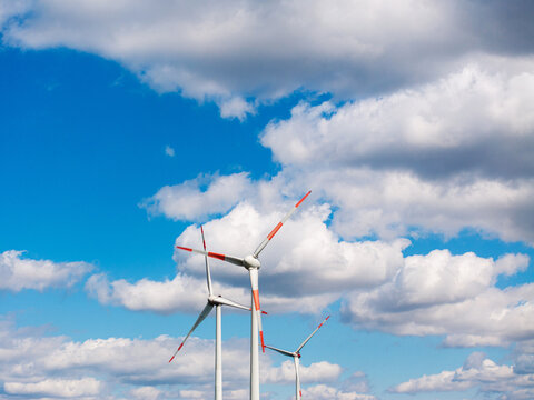 Aerial view of wind turbines in a wind park set against a bright blue sky with fluffy white clouds, Germany.