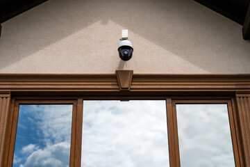 Outdoor security camera mounted above house windows reflecting cloudy sky, home surveillance system © Viktor Brazhnikow