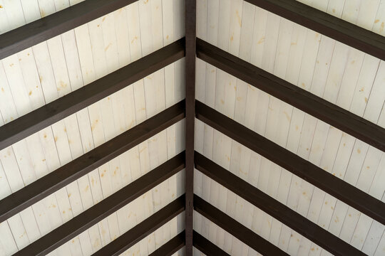 Interior view of a pitched wooden roof structure with exposed dark timber rafters and light wood paneling, construction detail of a residential attic or roof space