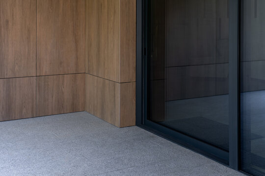 Modern entrance corner featuring wood cladding and dark glass sliding door, contemporary building exterior close-up photo