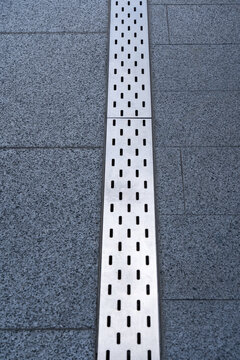Modern linear floor drainage system with brushed stainless steel grate set into textured stone tile flooring, architectural construction and waterproofing detail