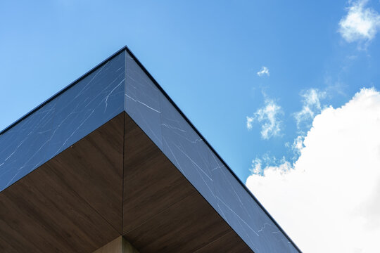 Sharp geometric corner of black marble building against blue sky with clouds, low angle architecture photo