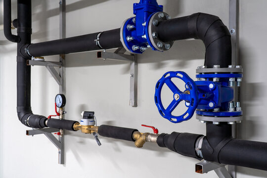 Industrial plumbing installation with pressure regulators, gauges, shutoff valve and blue water filtration components mounted on a wall