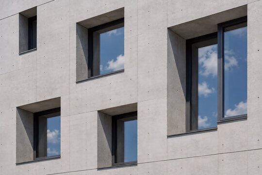 Moderne Sichtbetonfassade mit tiefen Fenstern und Himmelsspiegelung