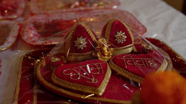 Close up of red velvet wedding tilak boxes embroidered with gold Devanagari script and small golden Ganesh idol wrapped in cellophane