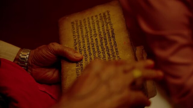 Close up of elderly hand holding ancient handwritten religious manuscript with Devanagari script during traditional Hindu wedding astrology reading