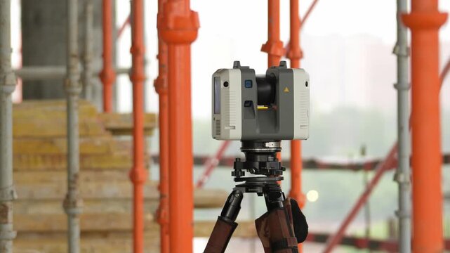 Gray laser level rests on a brown tripod. Orange scaffolding forms the backdrop. Concrete steps lead toward the site. This is a construction survey setting. Perfect for engineering projects