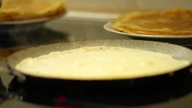 Pancake on a hot frying pan close-up. Cooking pancakes. Pan with a pancake and a plate with a stack of pancakes.