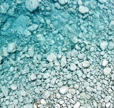 Clear turquoise water background showing pebbles stony riverbed pattern